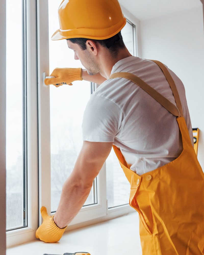 Handyman in yellow uniform installs new window. House renovation conception